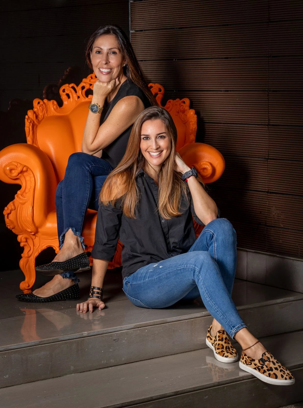 Sabri y Naty, fundadoras de Area Deco, sentadas junto a un sillón naranja