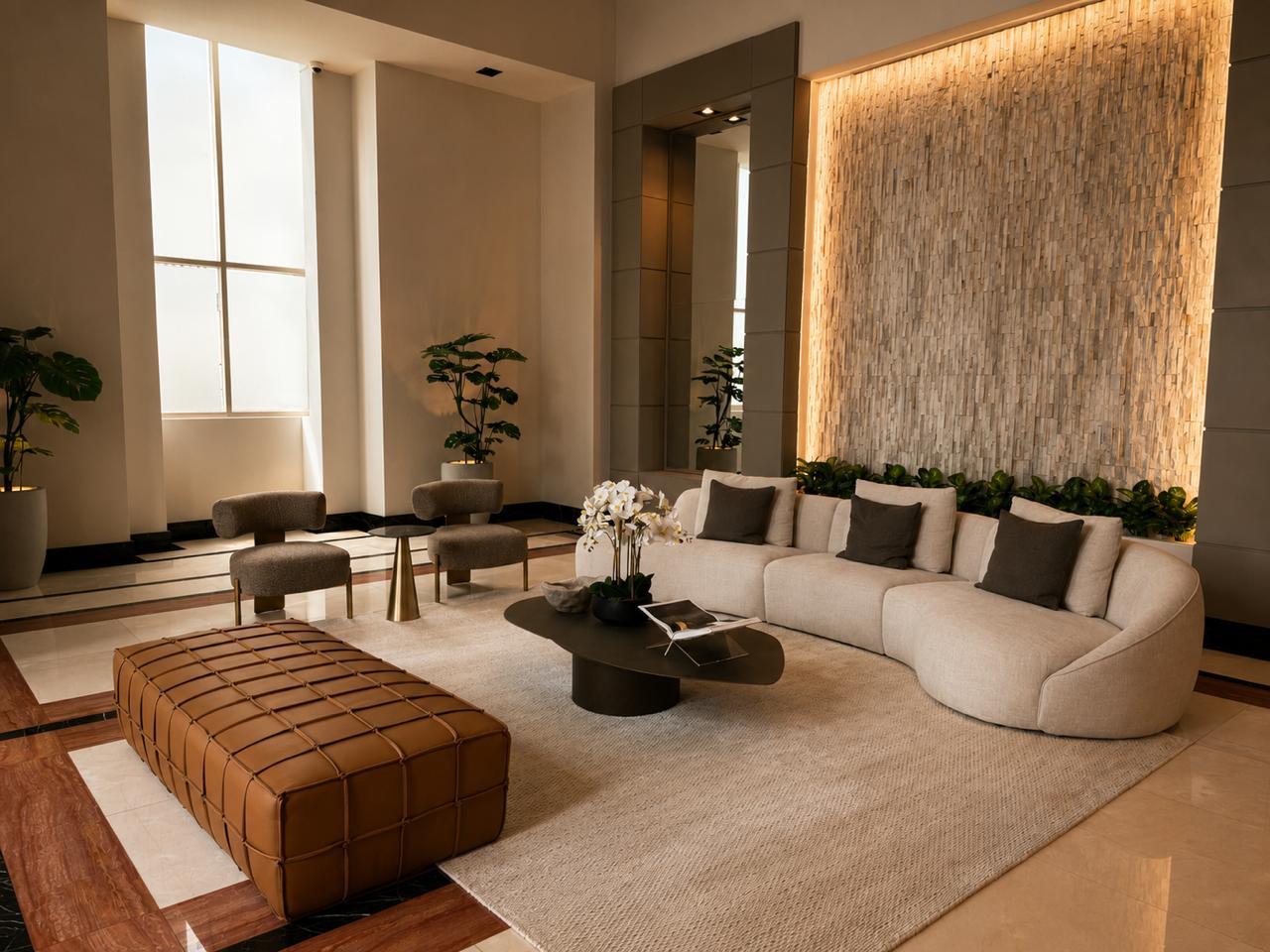 Sala de lobby con muro de piedra retroiluminado, sofá curvo color crema y otomana de cuero